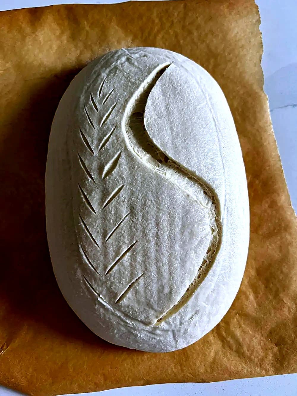 A hand-scored sourdough loaf with a wheat-stalk pattern, ready for the oven